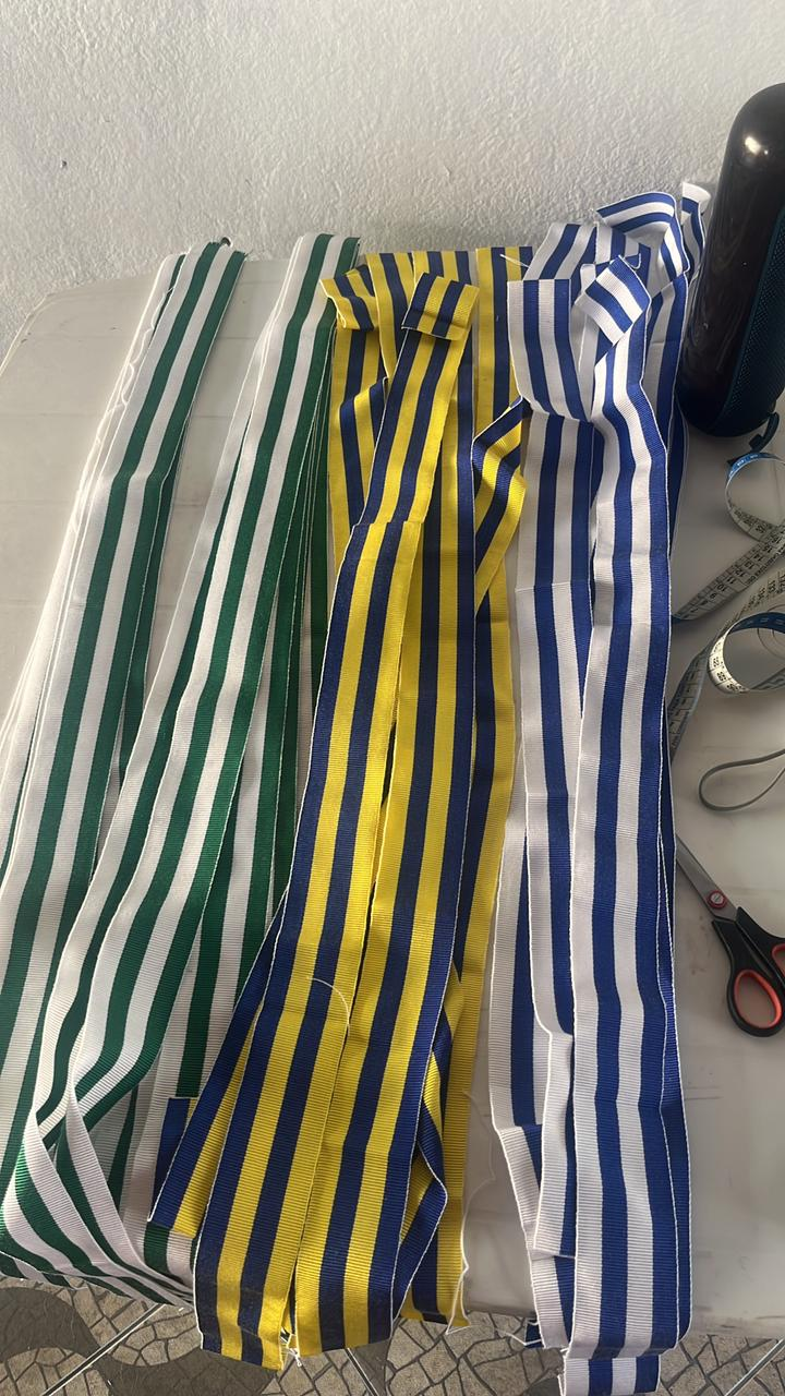 Várias fitas de gorgurão para cuíca lado a lado, em verde e branco, azul e amarelo e azul e branco